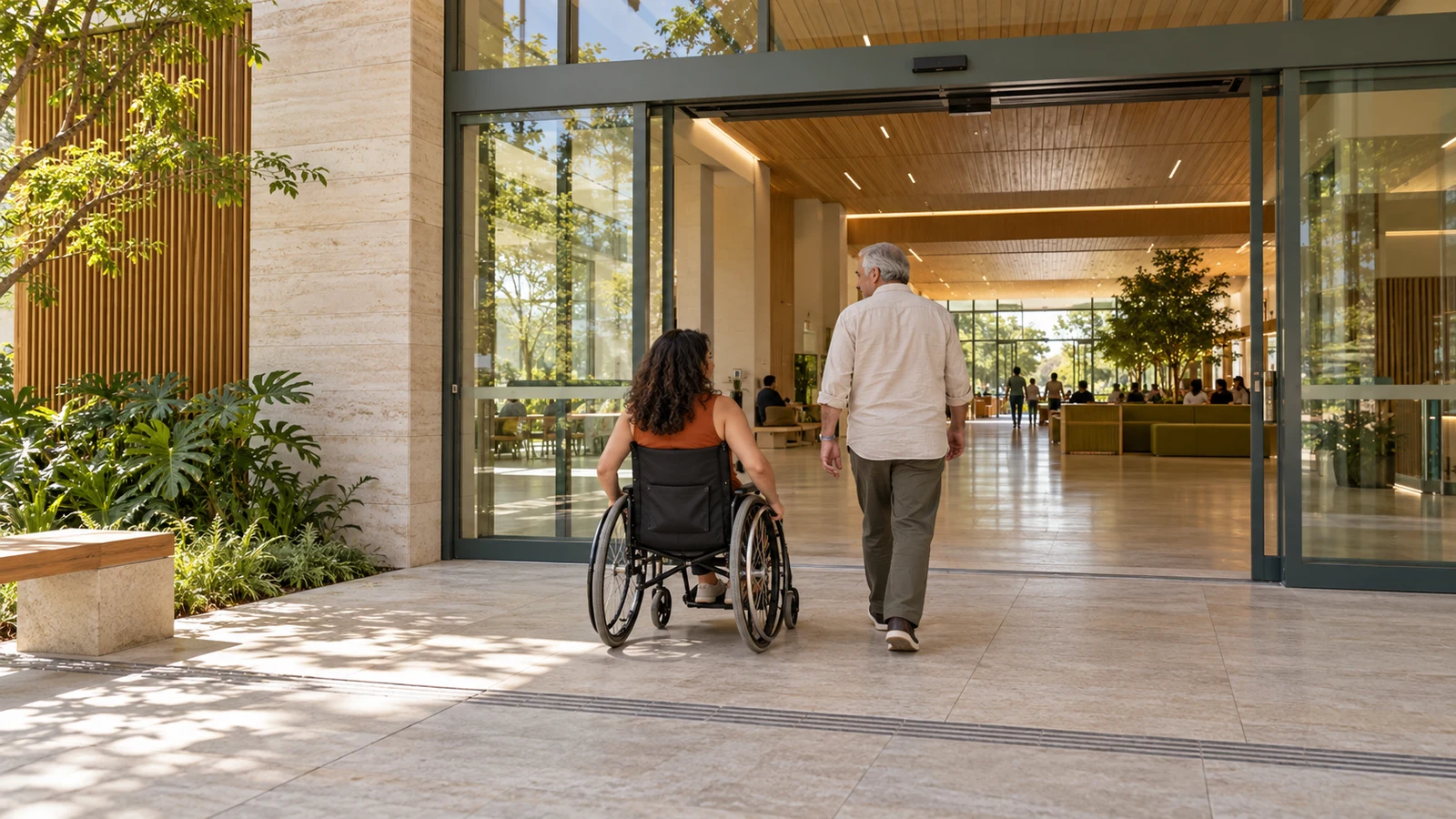 Woman in a wheelchair and elderly person entering through a stepless entrance